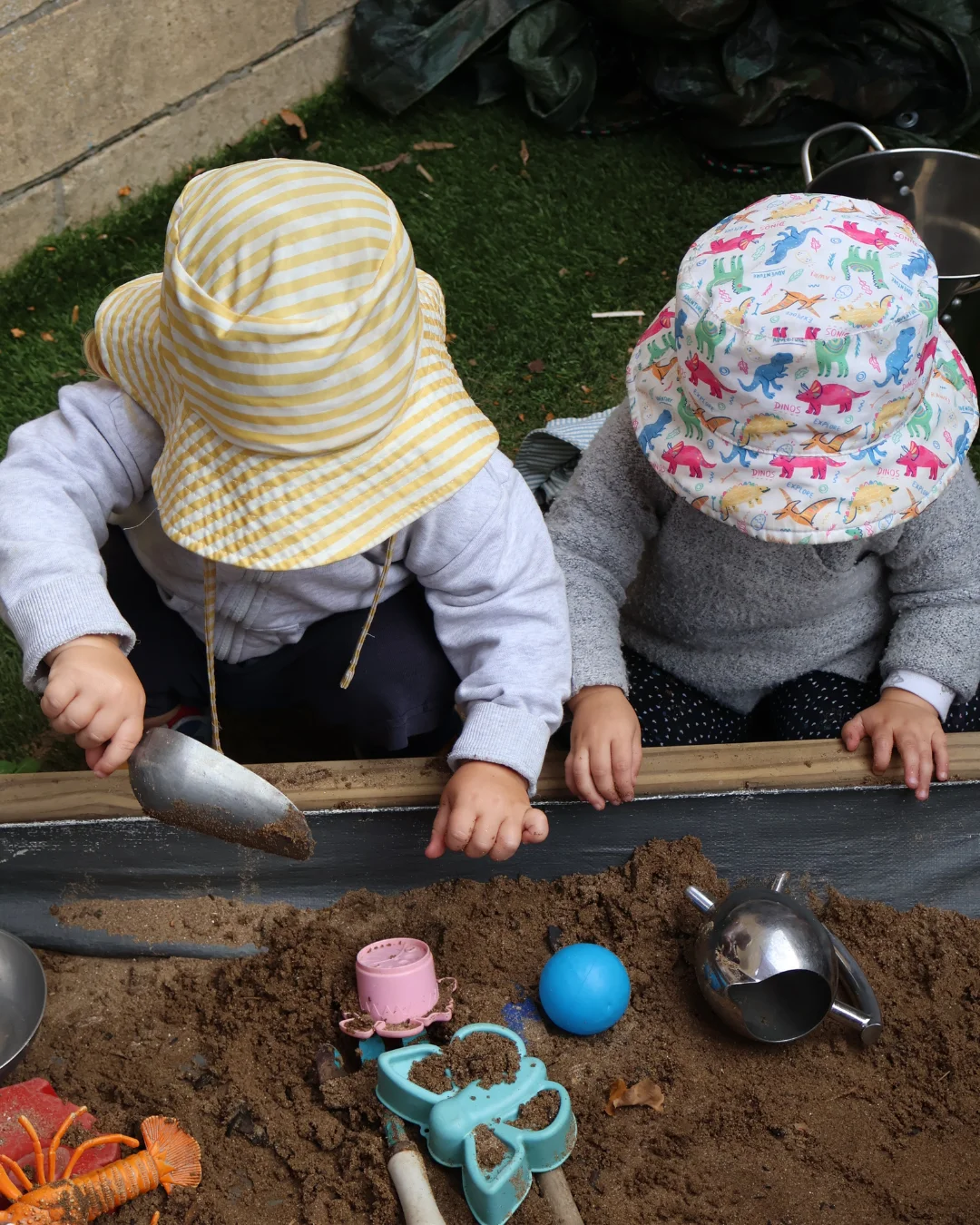 Two children in sun hats digging together in the sandpit