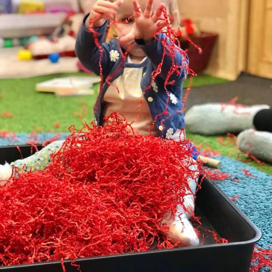 A child exploring red shredded paper during sensory play at Midsomer Norton